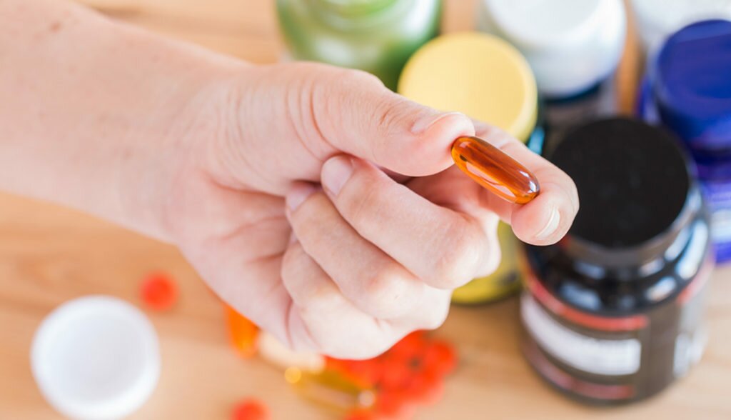 Close up of hand is holding a vitamin supplement on medicine bottles background. Medicine and health care concept.